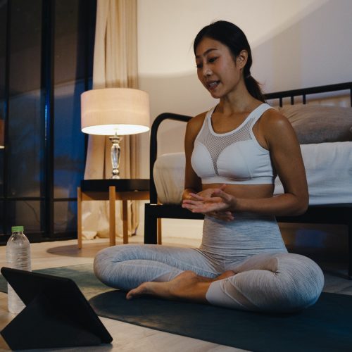 Young Asia lady doing work out and using tablet to watch yoga video tutorial at home night.